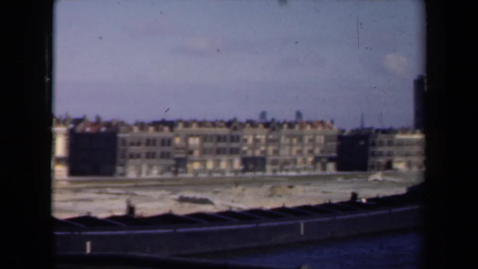 1946 Netherlands 8mm view of damaged or weathered waterfront buildings beyond bare sand or mud, with no visible people.