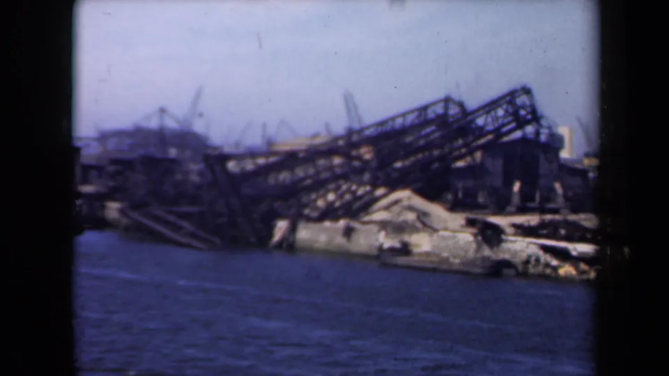1946 Netherlands 8mm frame showing a collapsed steel structure and debris along a waterfront, with blue water in the foreground.
