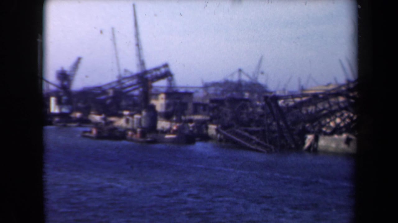 Shipyard waterfront with cranes, industrial buildings, and dark metal structures beside the water.