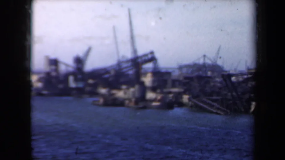 Blurred 1946 Netherlands shipyard frame with rippled water, crane silhouettes, dock buildings, and dark metal framework under a bright sky.