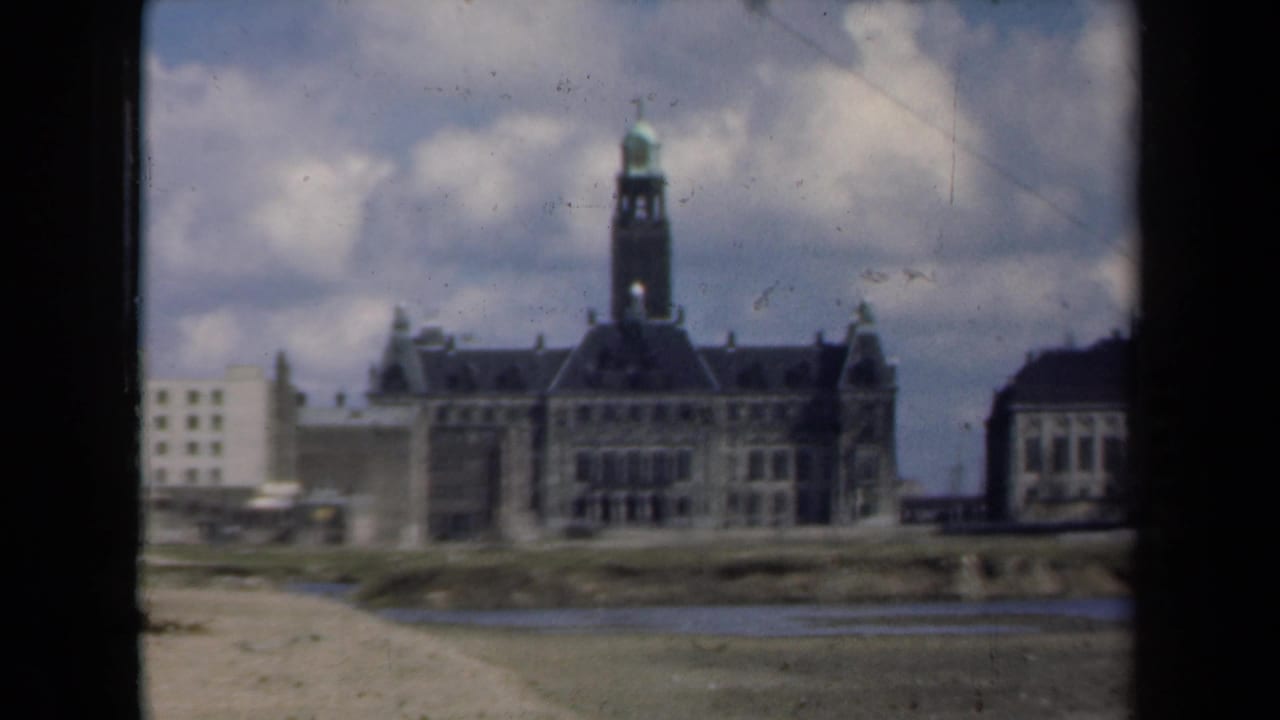 Large towered building beside a pale block structure across the water.