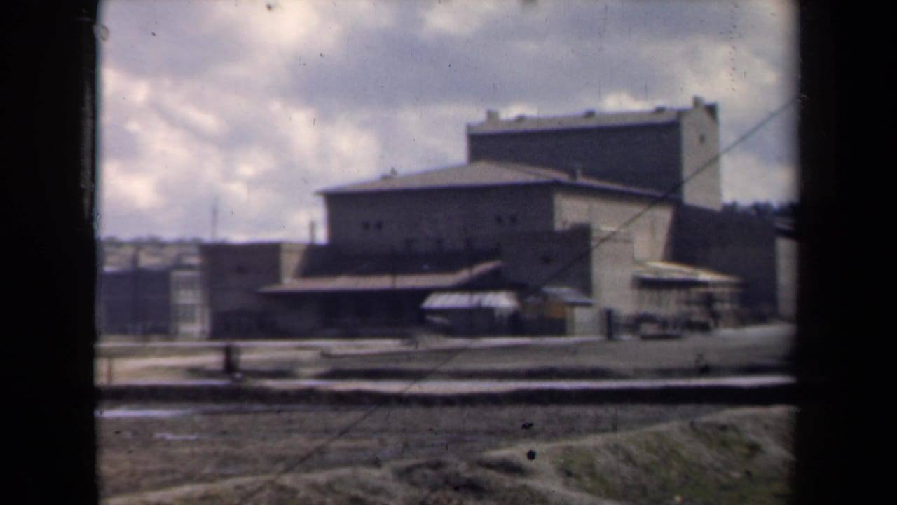 Flat-roofed building complex with awnings and an open muddy area in front.