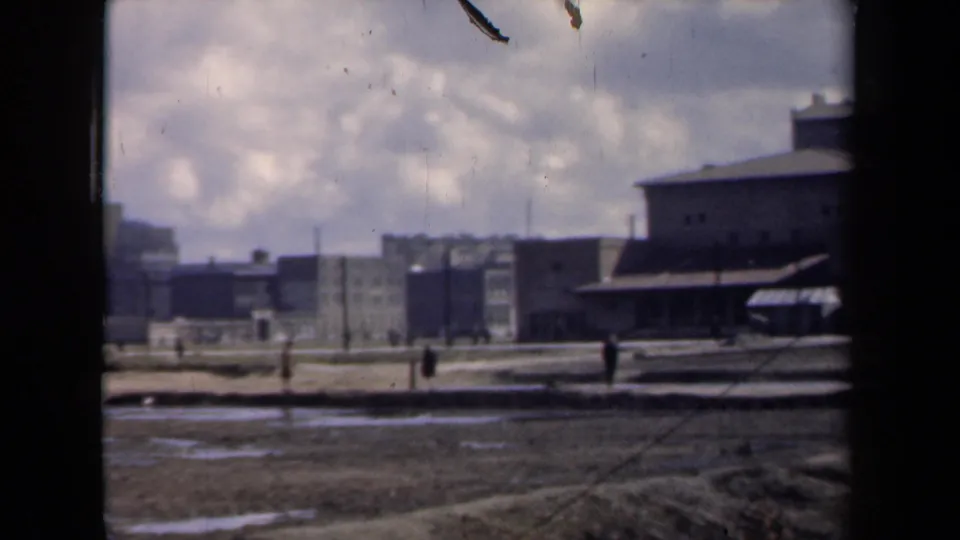 1946 Netherlands frame showing distant figures near a broad muddy courtyard and utilitarian buildings, partially obscured by the window frame.