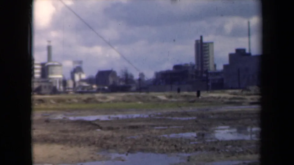 1940s home-movie view of wet ground facing industrial buildings and smokestacks in the Netherlands.