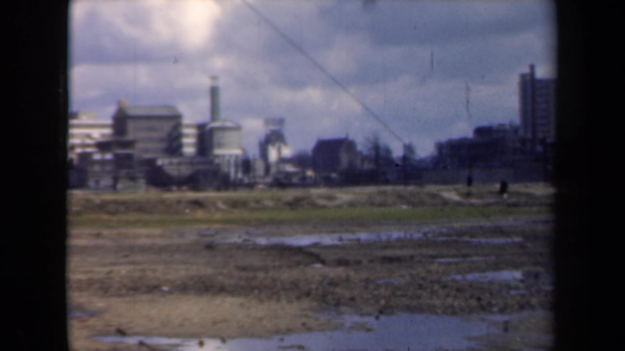 1946 Netherlands 8mm frame showing wet open ground in the foreground and a distant industrial skyline with smokestacks beyond.
