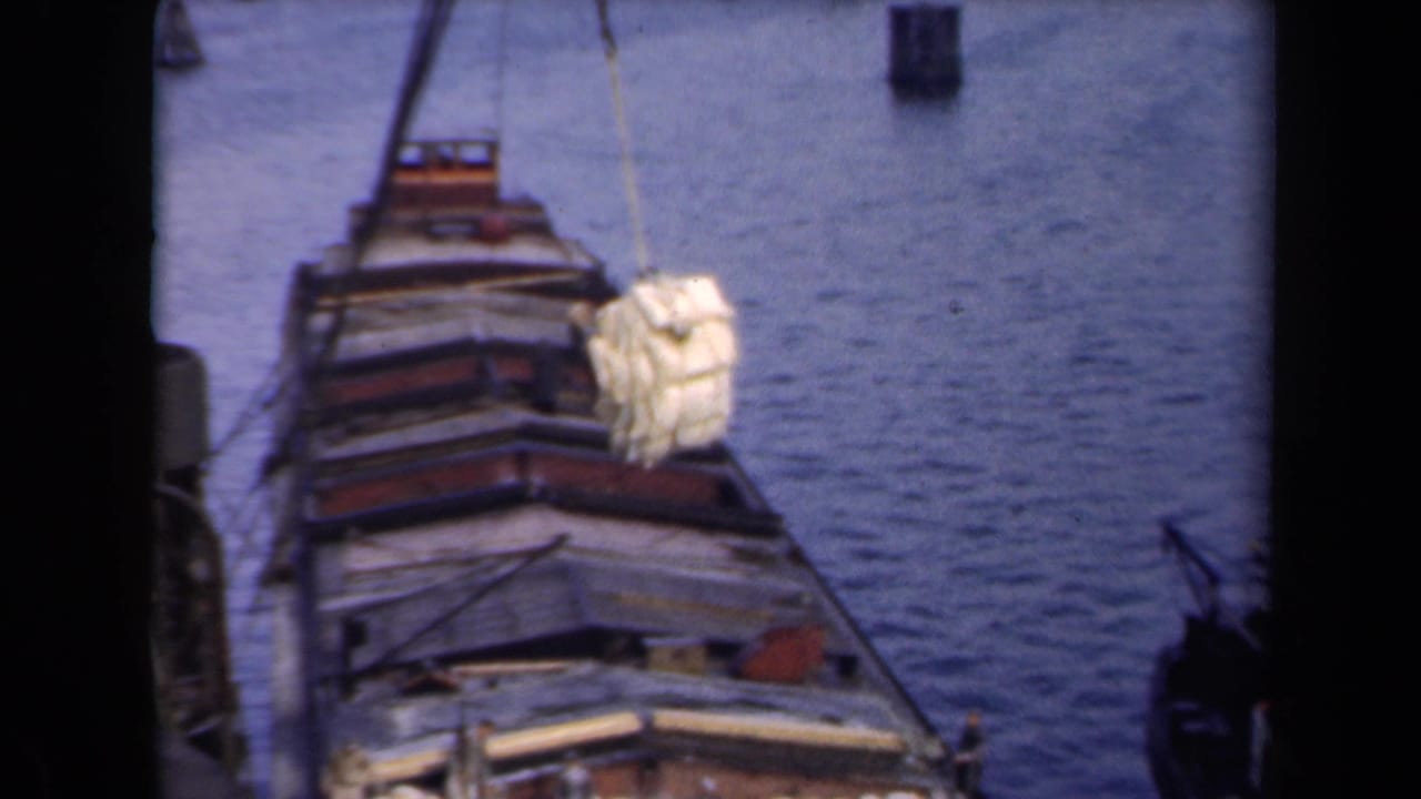1946 Netherlands 8mm frame showing a docked cargo vessel as a yellow bundle hangs from a rope above the open deck.