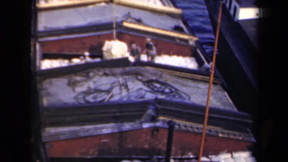 1946 Netherlands frame with a large pale sack being moved on a wooden barge as nearby workers stand among cargo and rope.