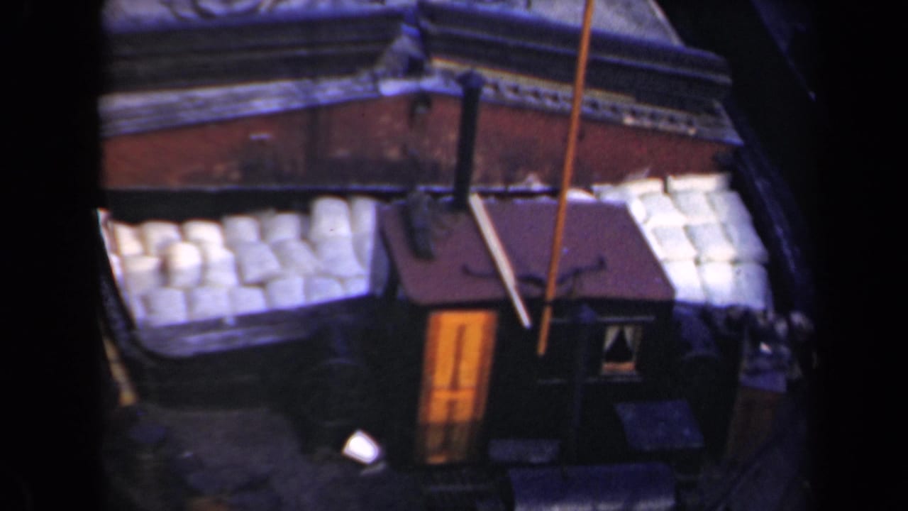 1946 Netherlands 8mm frame showing an elevated view of a vessel or waterside deck area with pale stacked objects, a small cabin, and dark water nearby.