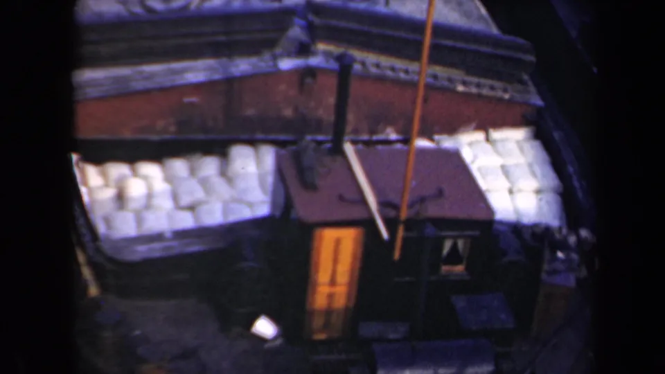 1946 Netherlands 8mm frame showing an elevated view of a vessel or waterside deck area with pale stacked objects, a small cabin, and dark water nearby.