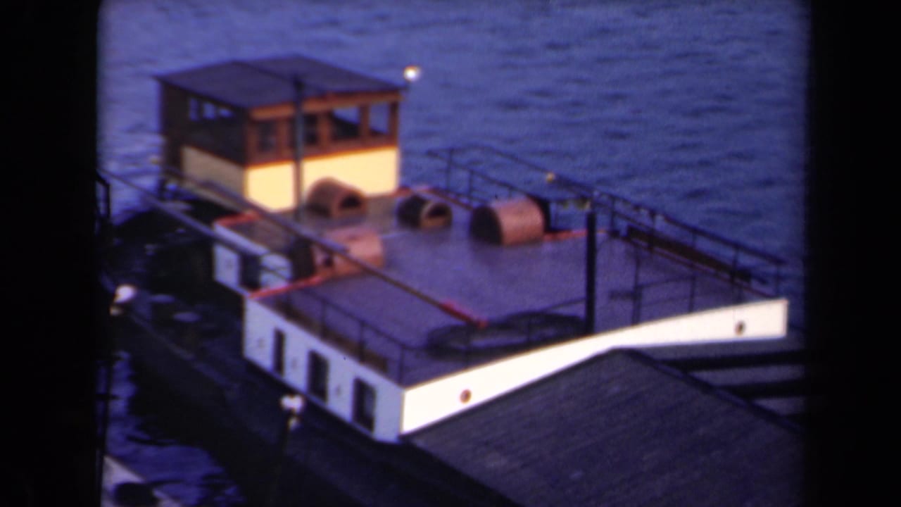 1946 Netherlands 8mm frame showing the small boat from above, with a wooden cabin, pale hull, deck railings, and calm surrounding water.