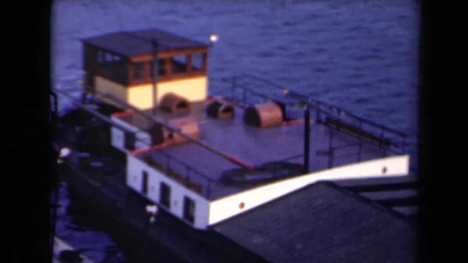 1946 Netherlands 8mm frame showing the small boat from above, with a wooden cabin, pale hull, deck railings, and calm surrounding water.