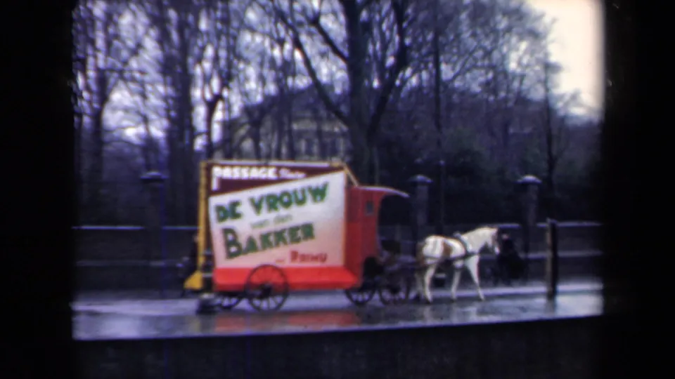 A white horse pulls a red and yellow Dutch advertising cart past bare trees on a wet Netherlands street in 1946 footage.