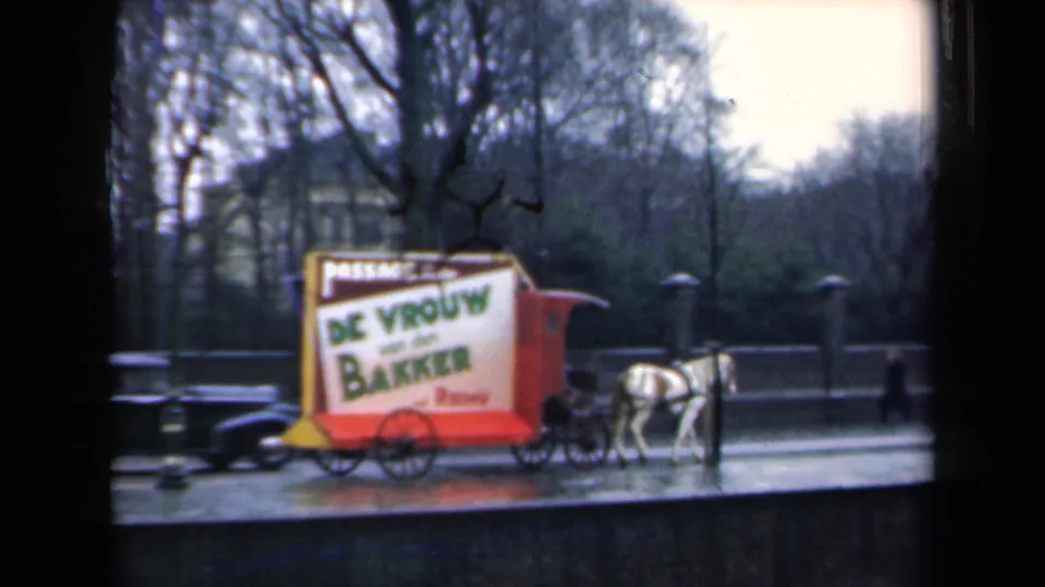 A horse-drawn advertising cart for De Vrouw van den Bakker shares a wet Dutch street with a dark car in 1946 footage.
