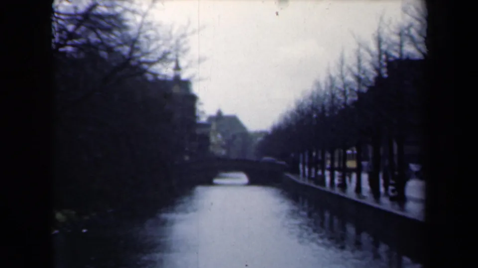 1946 Netherlands frame of the Peace Palace canal approach, with rows of leafless trees, reflective water, and a low bridge in the distance.