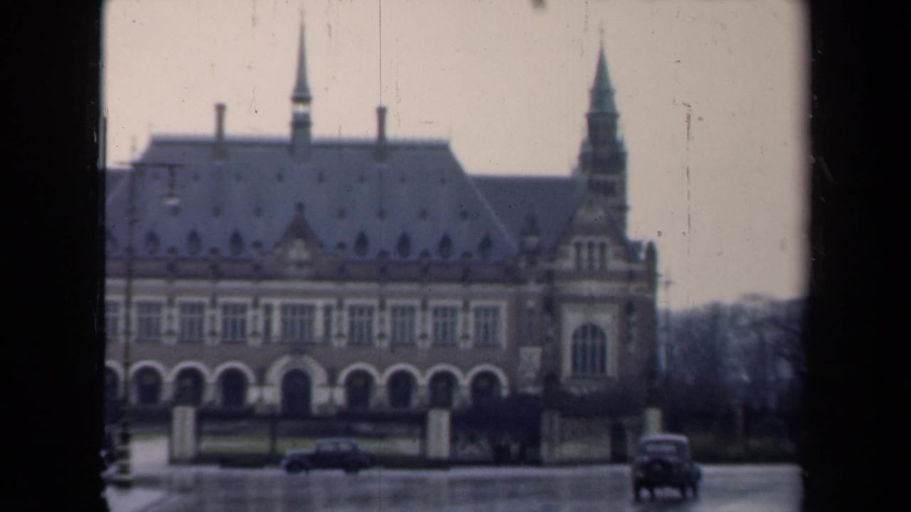 1946 Netherlands 8mm view of a large ornate building seen across a wet street, with cars and dark frame edges visible.