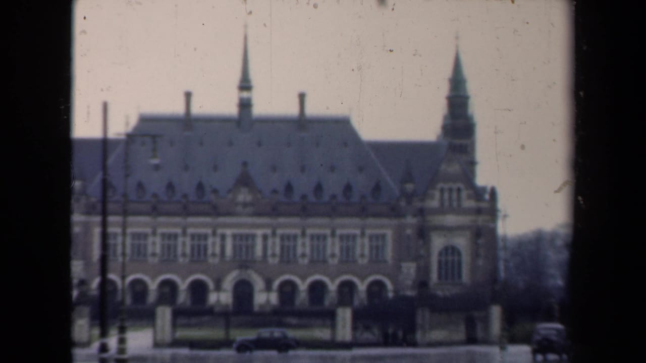 Large historic building with twin pointed roof features and cars on a wet road.