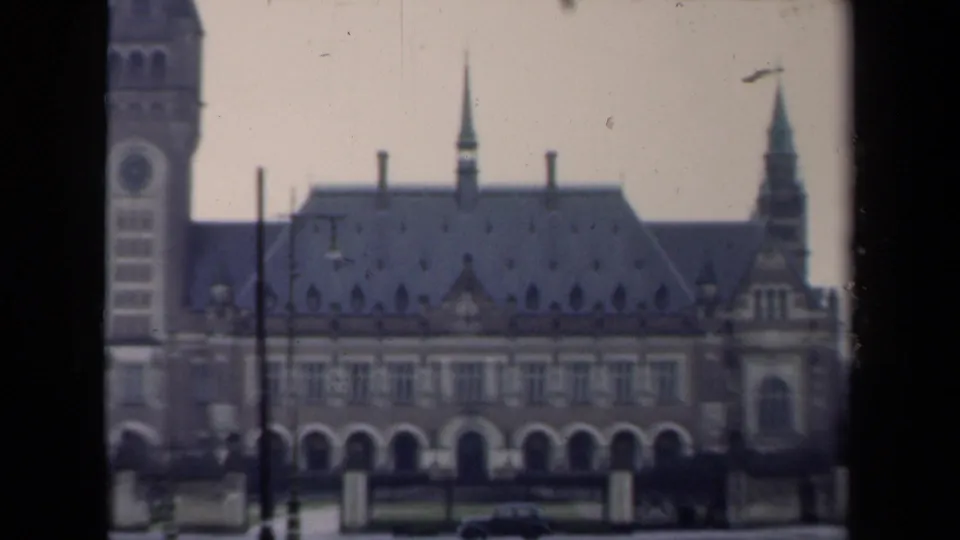 1946 Netherlands 8mm frame with a partial tower, ornate roofline, wet pavement, and a car in front of the building.
