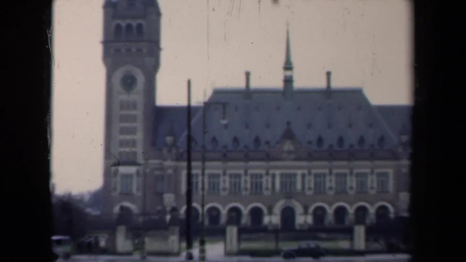 1946 Netherlands home-movie view of a towered historic building across a wet street, with a car and film-edge framing.