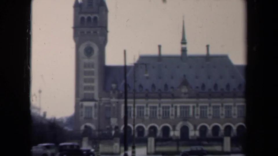 1946 Netherlands 8mm frame showing a formal historic building with a clock tower, arched facade, parked cars, and overcast sky.