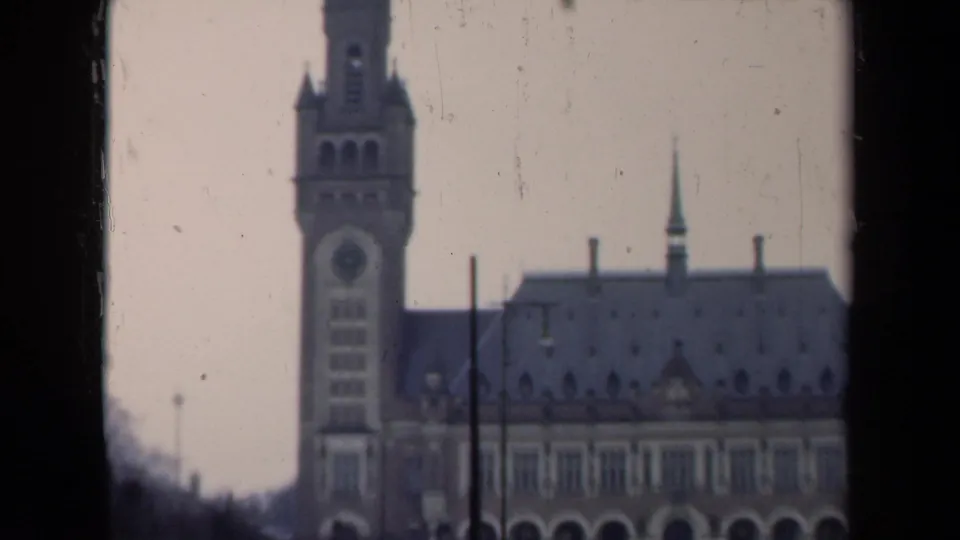 1946 Netherlands view of a large masonry building with a clock tower, steep roof, lamp posts, and visible film grain.