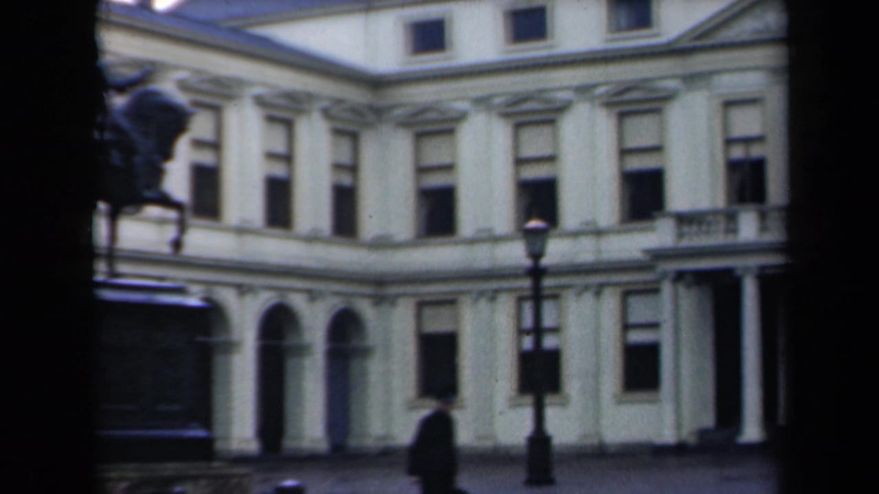 Classical building facade with arched windows, streetlamp, and a dark-clothed pedestrian walking past.