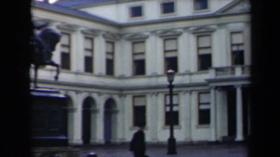1946 Netherlands frame with a formal building facade, arched ground-floor openings, streetlamp, and distant pedestrian crossing the foreground.