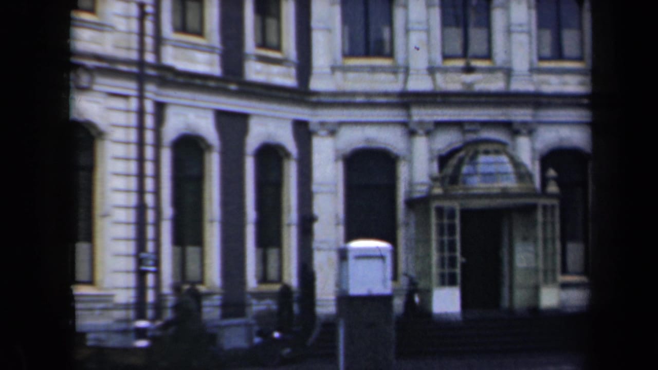1946 Netherlands home-movie frame showing a grand stone building facade with arched windows, columns, steps, and a glass-covered entrance.