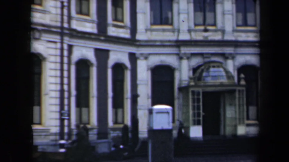 1946 Netherlands home-movie frame showing a grand stone building facade with arched windows, columns, steps, and a glass-covered entrance.