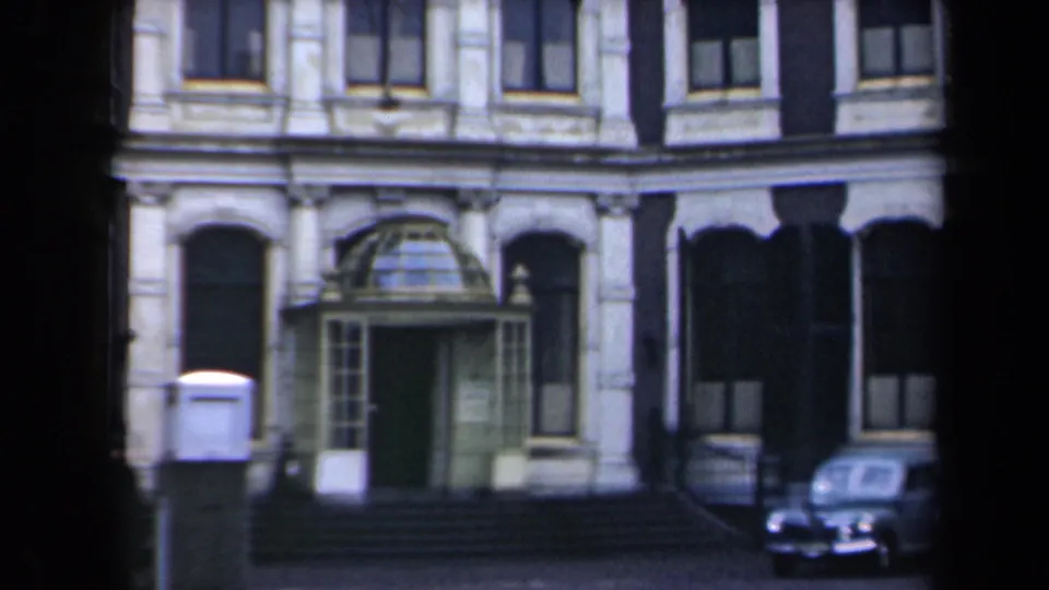 1946 Netherlands 8mm frame with a formal building entrance, iron railings, and part of a rounded 1940s-style sedan at street level.