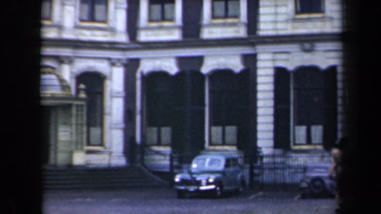Ornate building facade with a parked vintage car and railings along the street.
