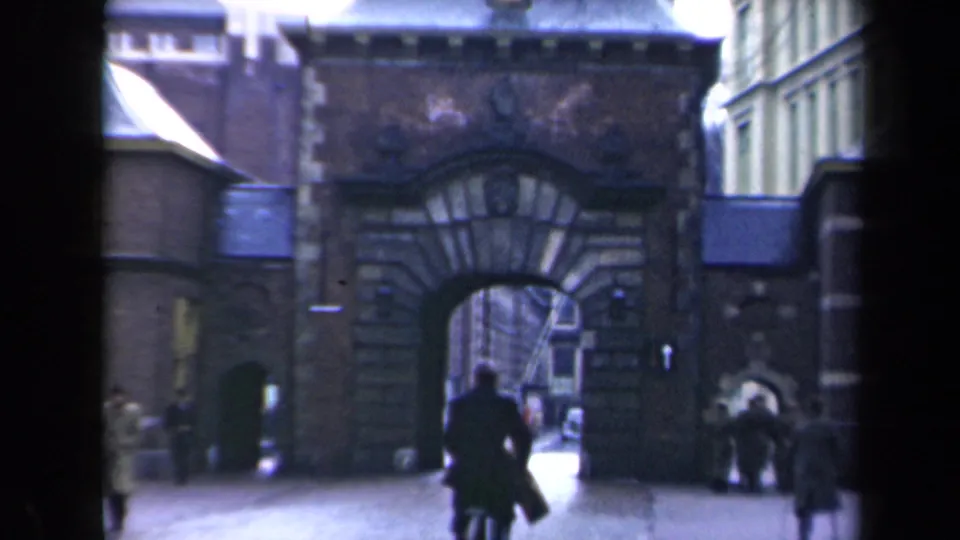 A large masonry archway frames a passage where pedestrians and bicycles move through an urban setting.