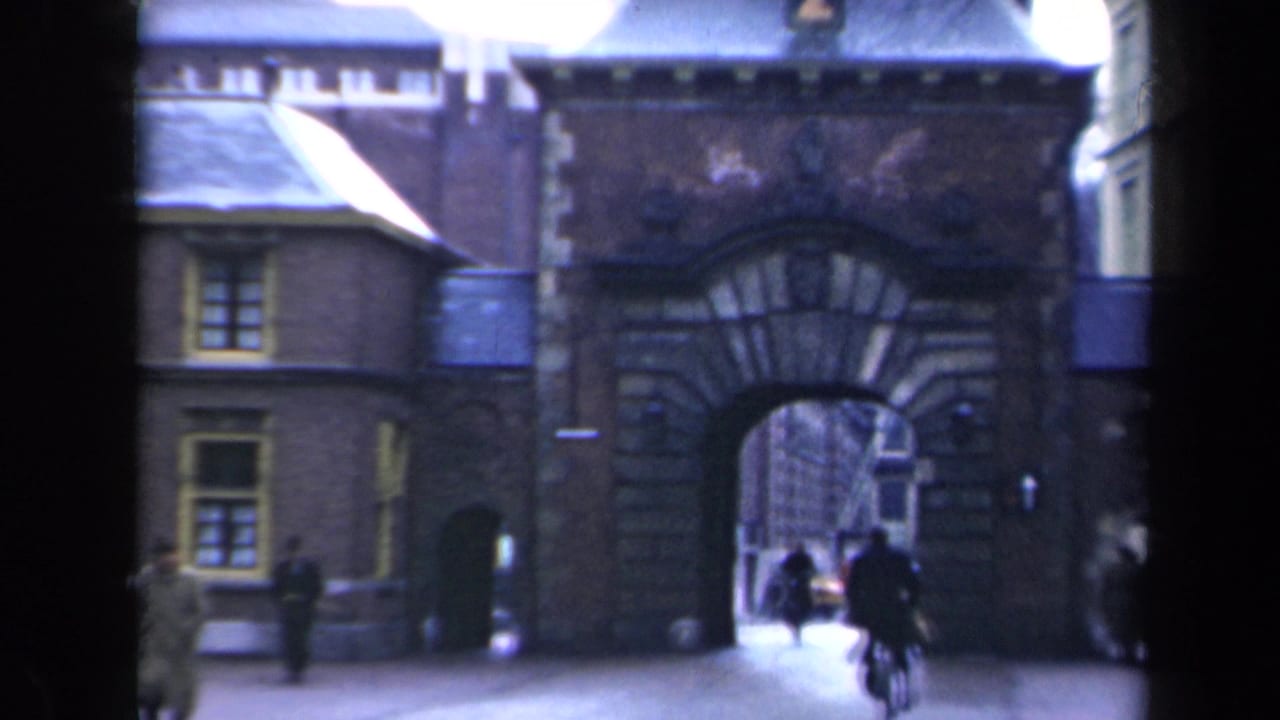 Stone gateway and adjoining buildings with a cyclist entering the arched passage.