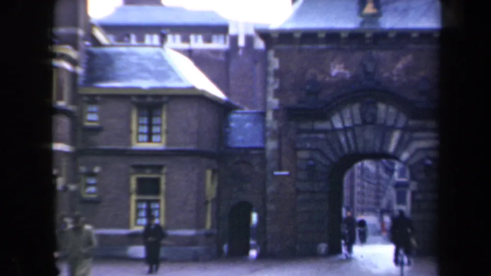 Closer 8mm view of the stone arch and neighboring building, with pedestrians moving near the street entrance.