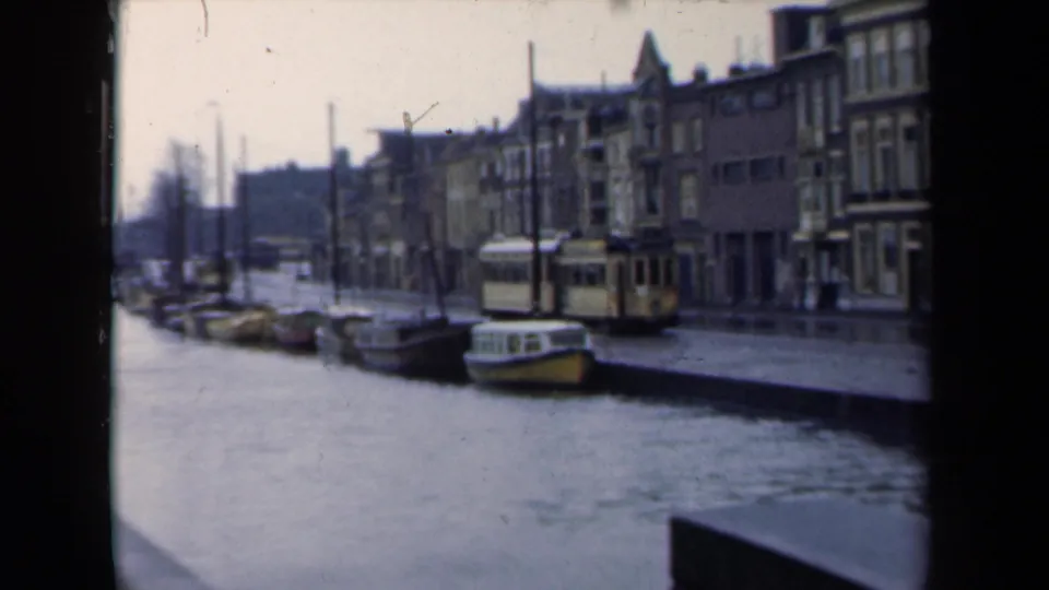 1946 Netherlands canal view with moored boats, a tram moving beside the water, and older streetfront buildings.