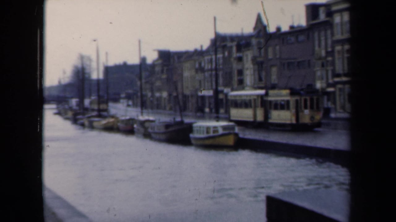 Tram beside a canal with boats and rows of buildings in the background.