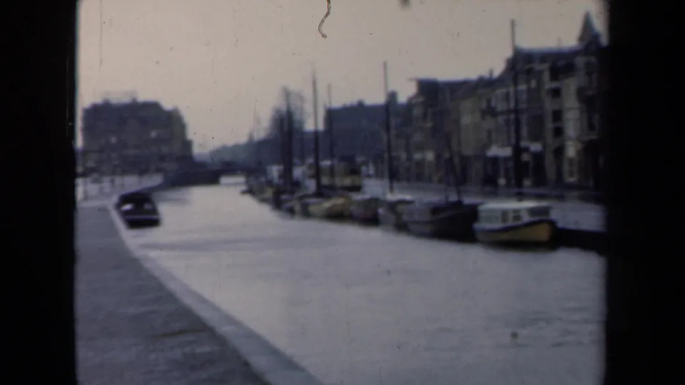 1946 Netherlands canal scene with moored boats, dense older buildings, bare trees, and a dark moving shape near the left bank.