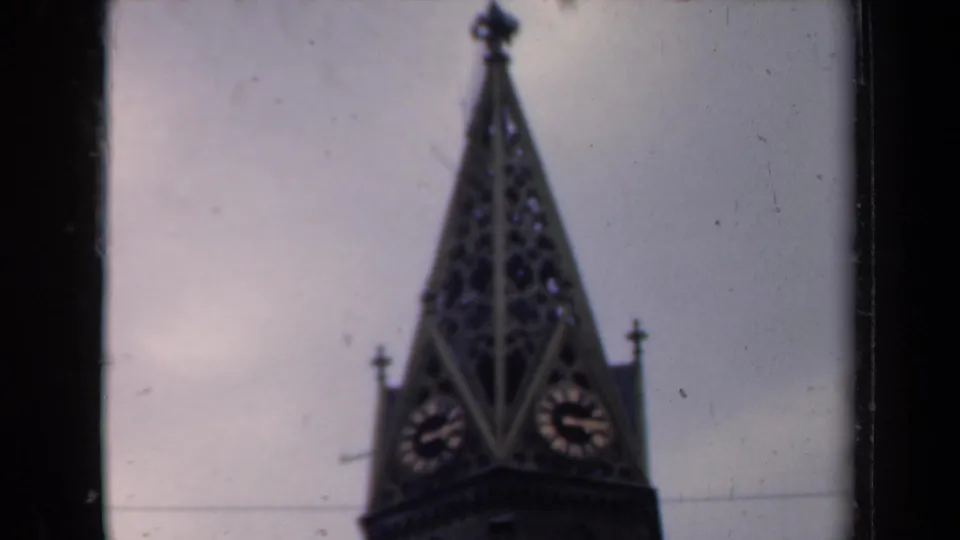 Soft 8mm frame of a tall clock-tower spire, likely in the Netherlands, with two visible clock faces and decorative roof details.