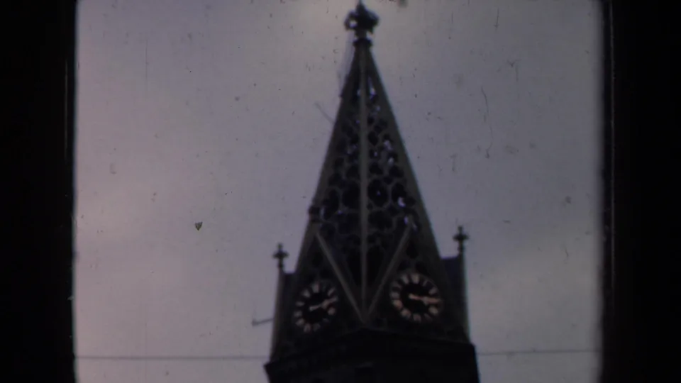 1946 Netherlands home-movie still showing the church spire lower in frame with clock faces and visible film wear.