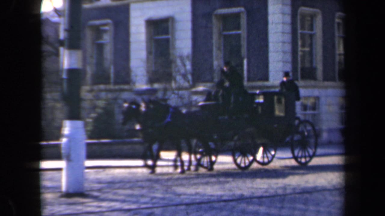 1946 Netherlands 8mm frame showing a horse-drawn carriage with two men moving past a masonry building and white roadside posts.