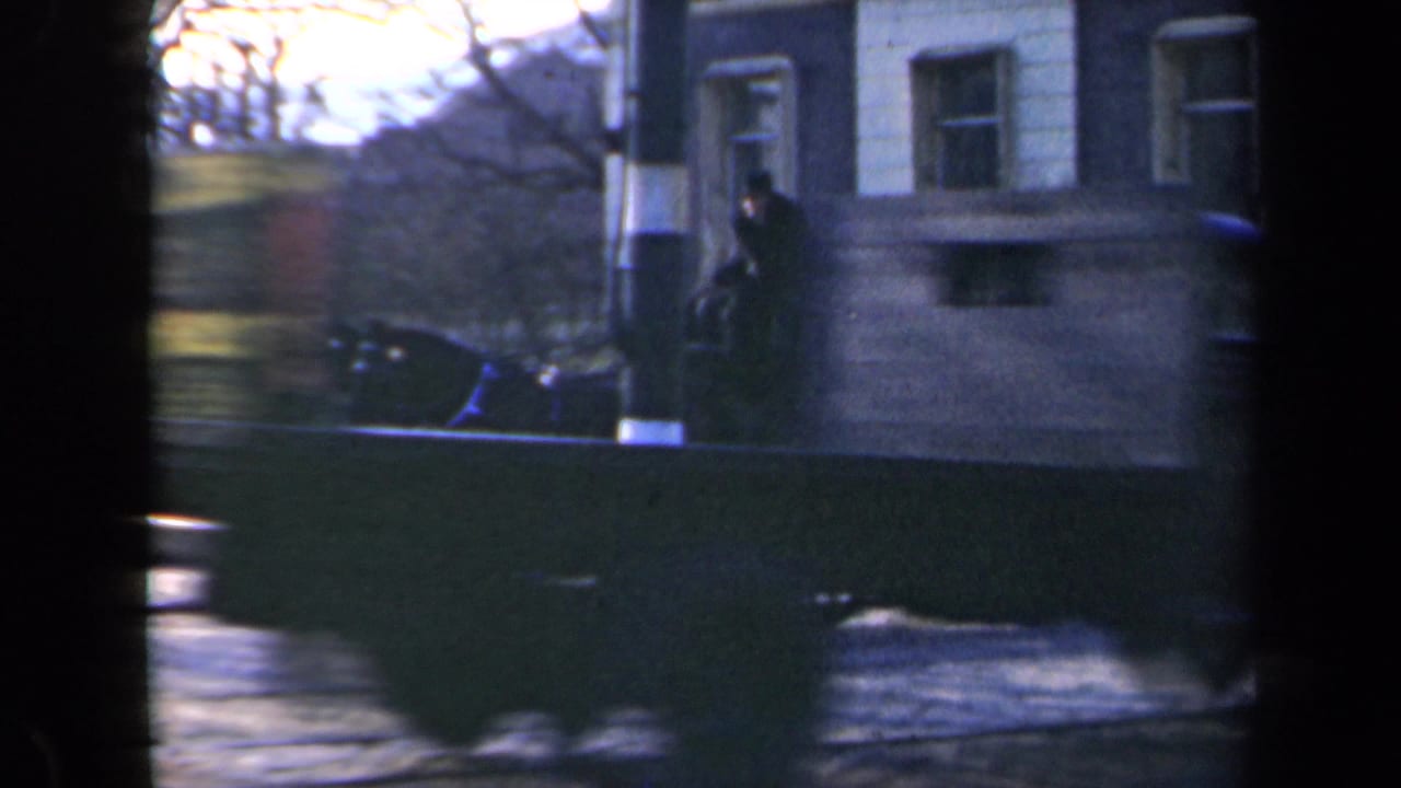Blurred carriage scene beside buildings with a dark vertical film edge in the center.
