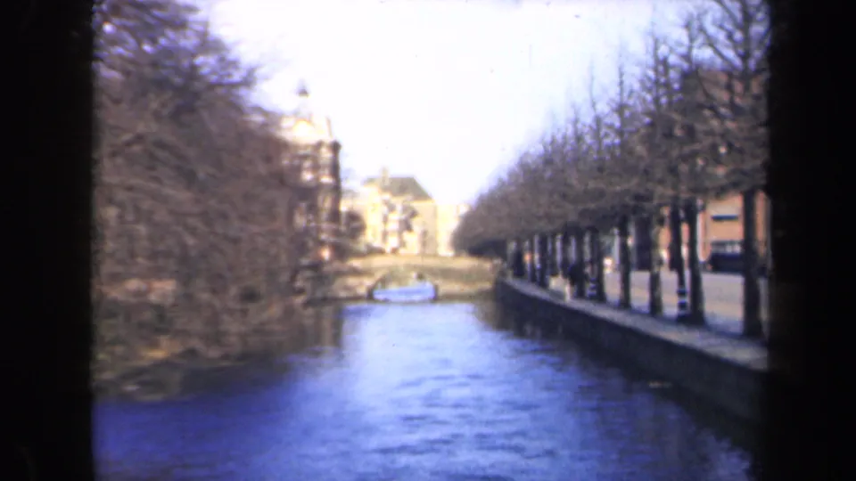 1946 Netherlands 8mm frame looking down a narrow canal bordered by bare trees, buildings, and reflected daylight.
