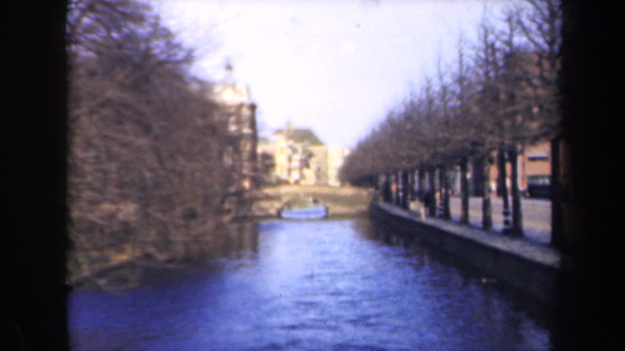 1946 Netherlands 8mm frame showing a canal lined with bare trees, waterside buildings, and a small distant boat.