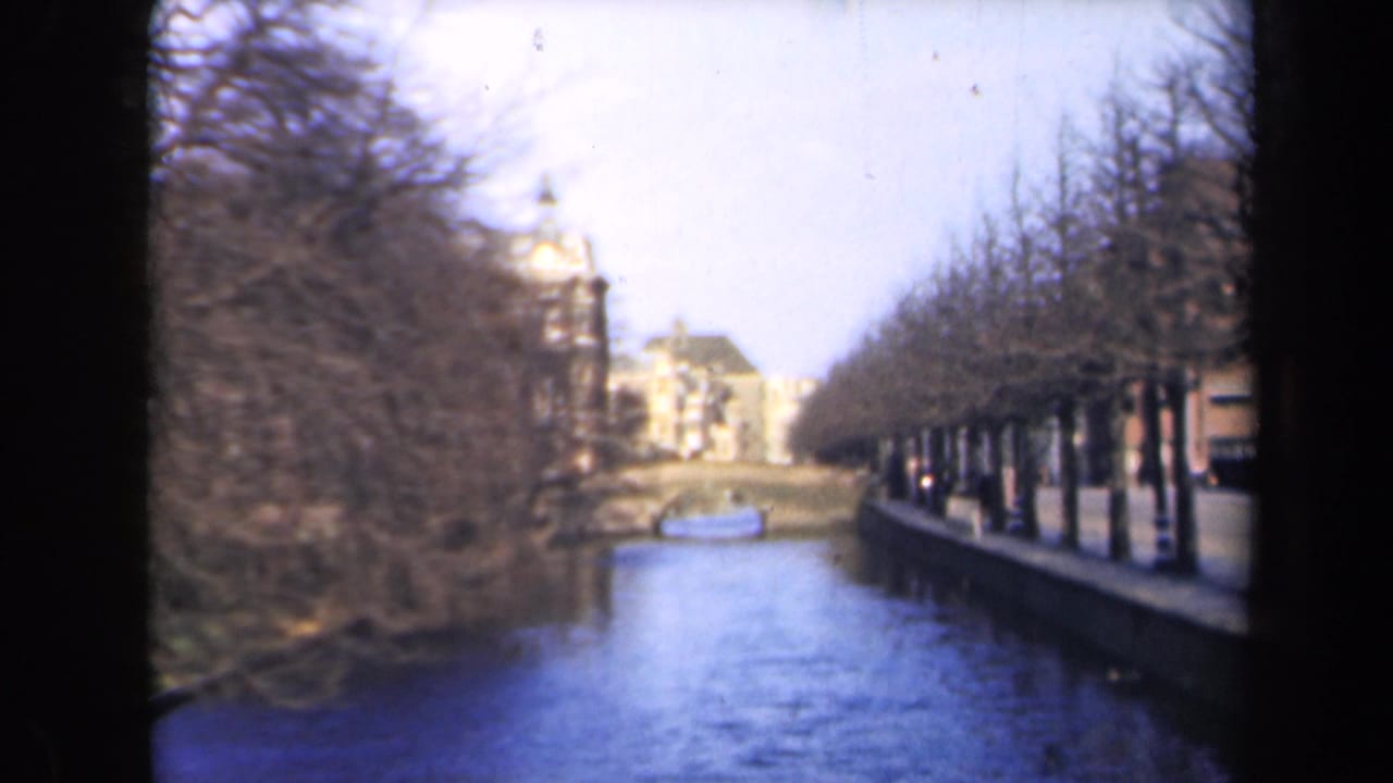 Tree-lined canal with distant buildings and a small boat near the center.