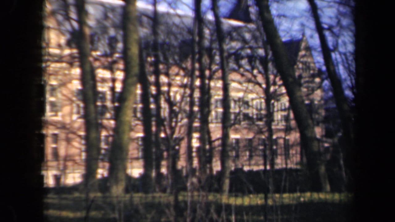 1946 Netherlands 8mm frame showing a large brick building seen through leafless trees and dark film borders.
