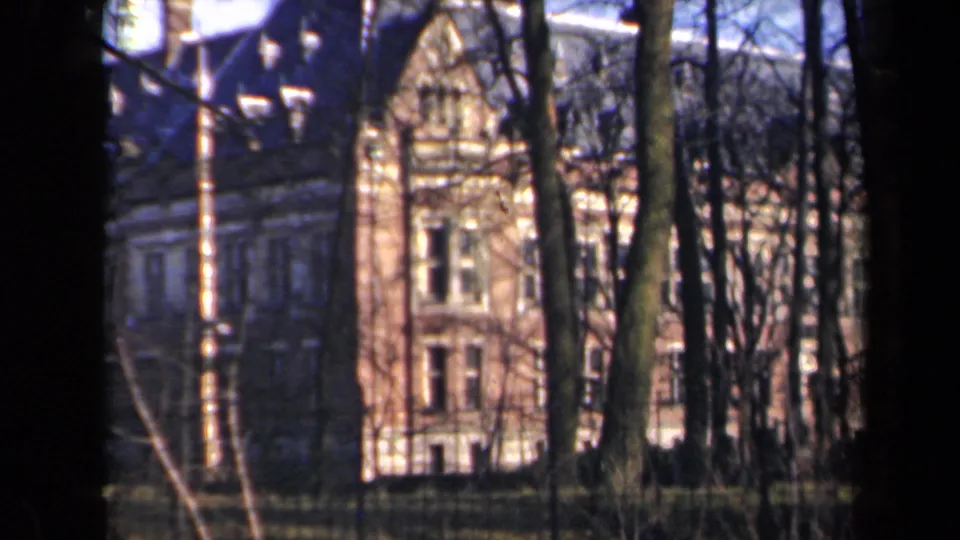 1946 Netherlands 8mm view of a large masonry building glimpsed through a stand of leafless trees.