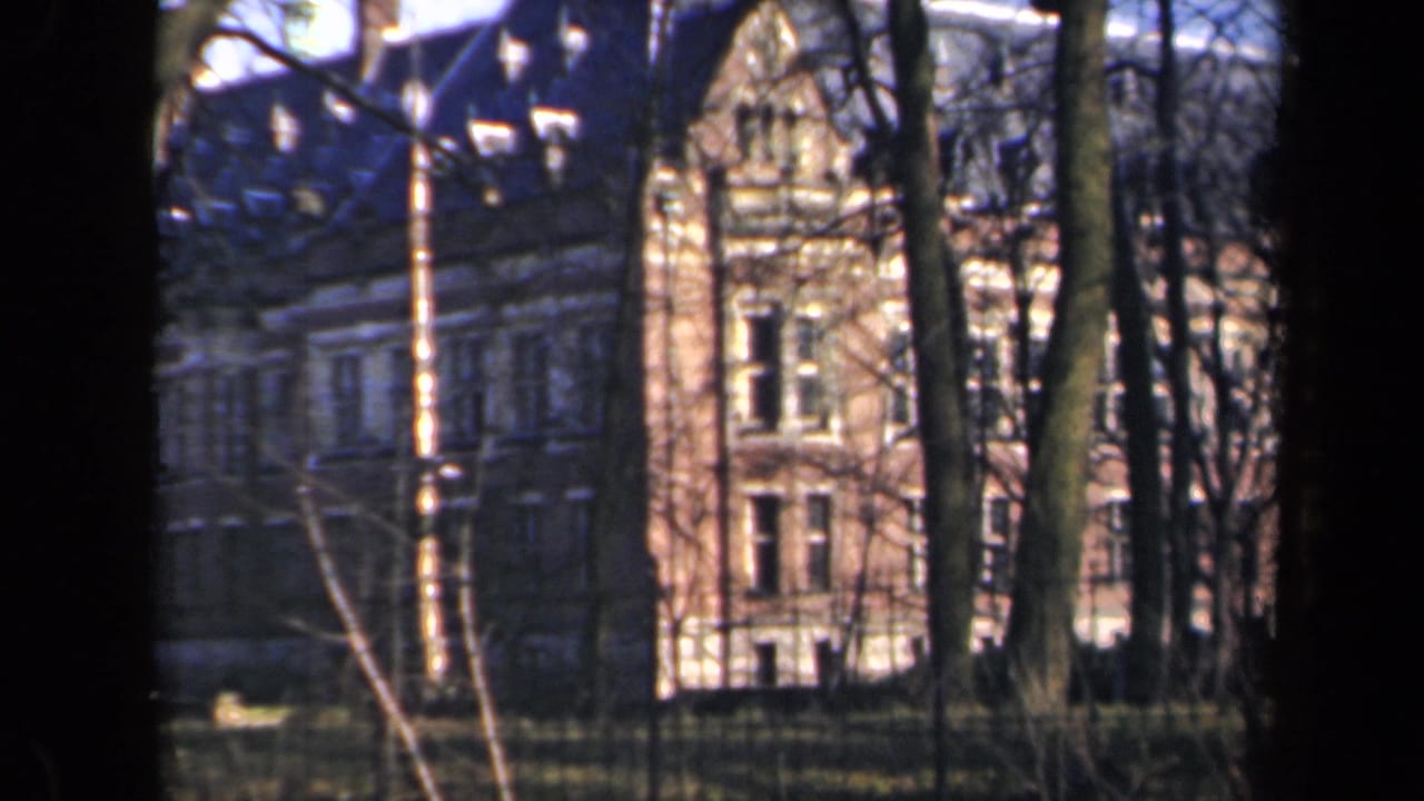 1946 Netherlands home-movie frame showing a large building with tall windows seen through leafless trees.
