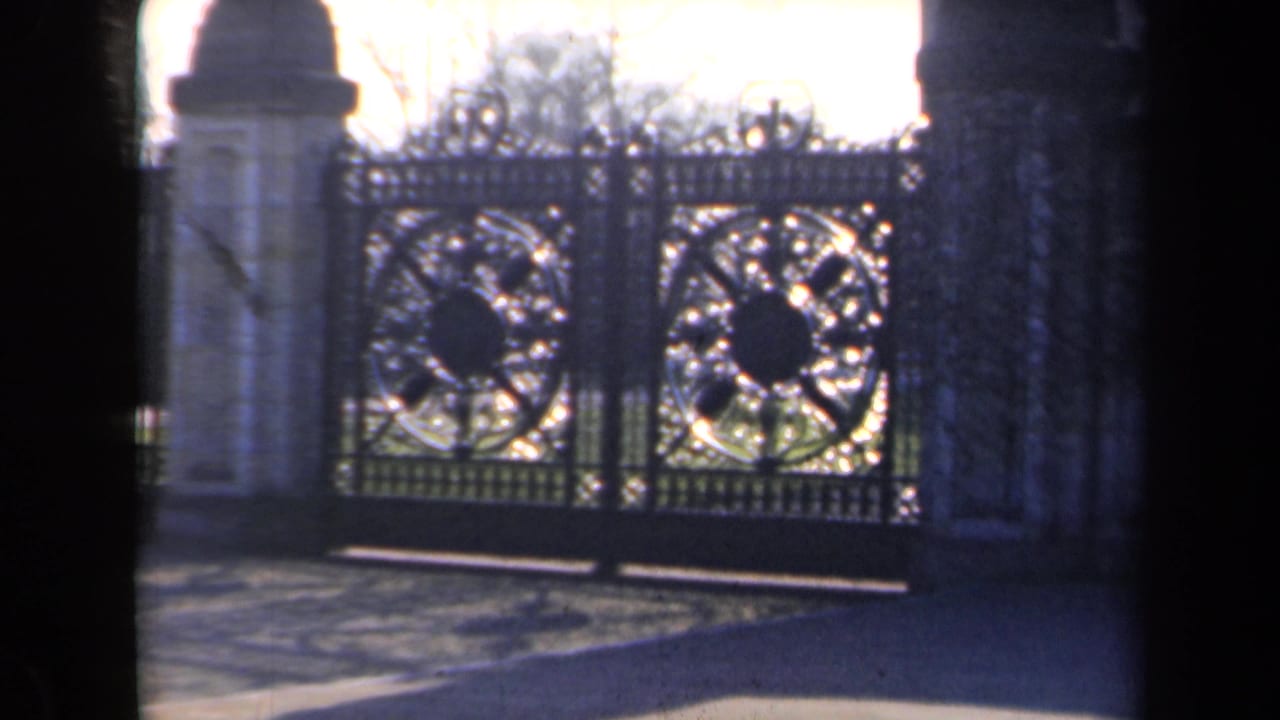 1946 Netherlands 8mm frame showing large decorative iron gates with circular ironwork, flanked by pale stone pillars and bare trees.