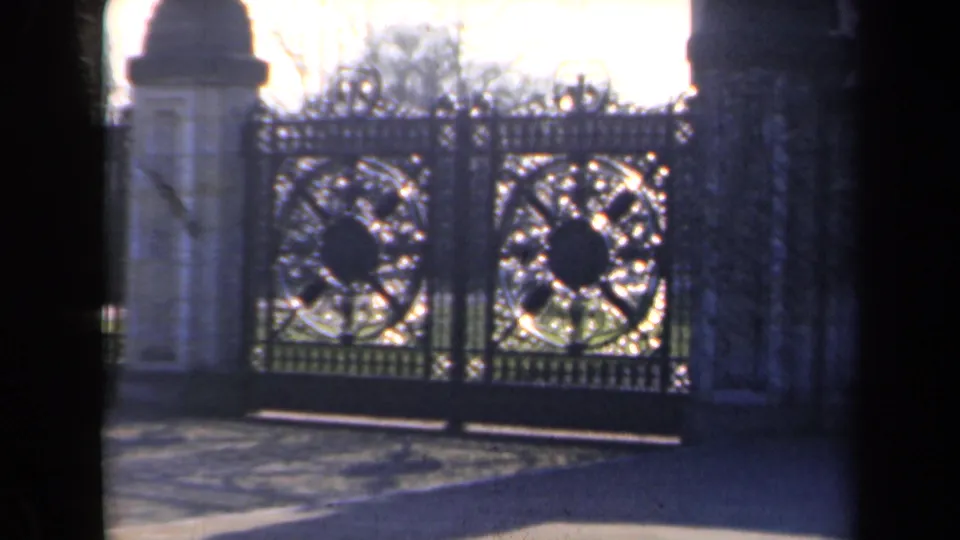 1946 Netherlands 8mm frame showing large decorative iron gates with circular ironwork, flanked by pale stone pillars and bare trees.