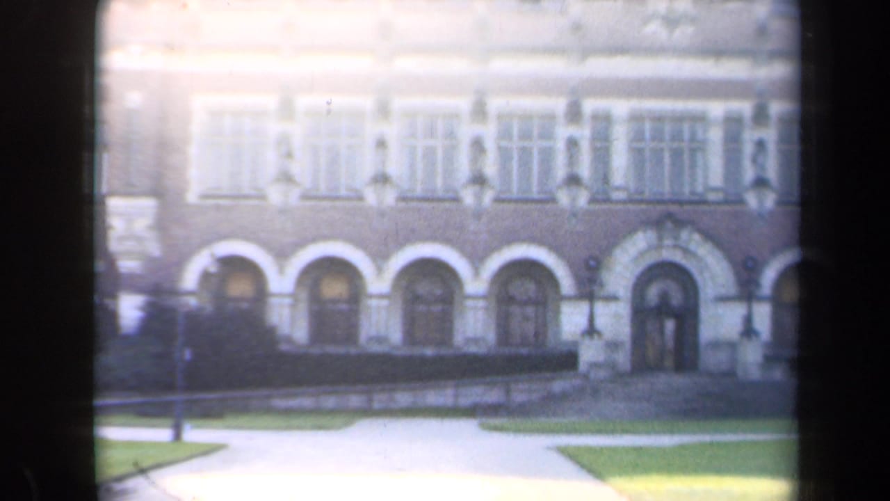Facade of a large masonry building with arched doors, upper windows, lawn, and path.