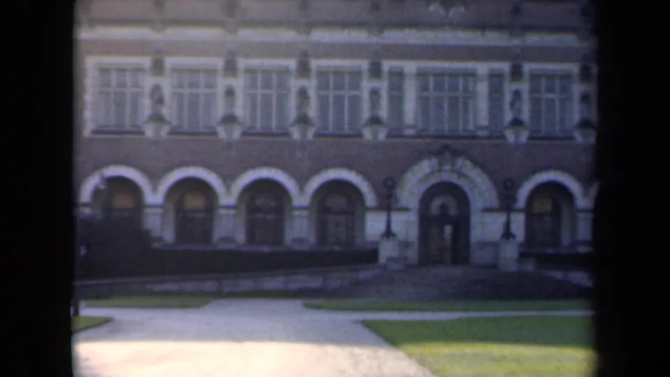 1946 Netherlands 8mm frame showing the lower facade of a formal building, including arched openings, window rows, hedges, path, and grass.